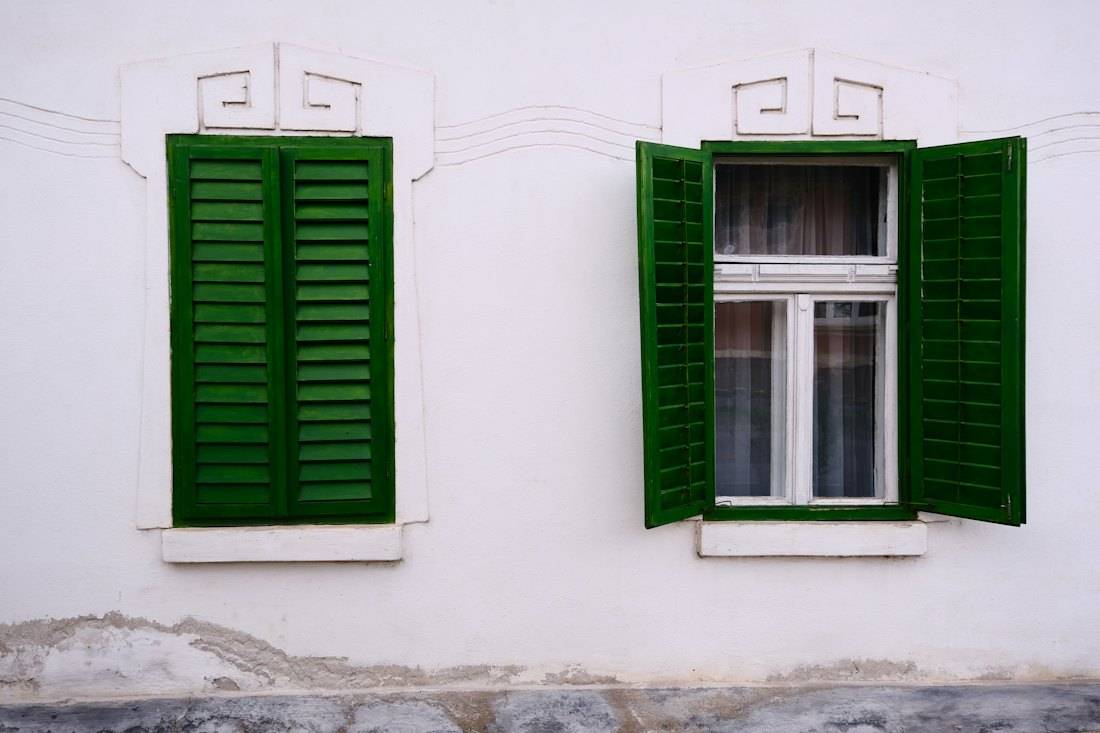 Fenêtre blanche à persiennes vertes sur une façade claire