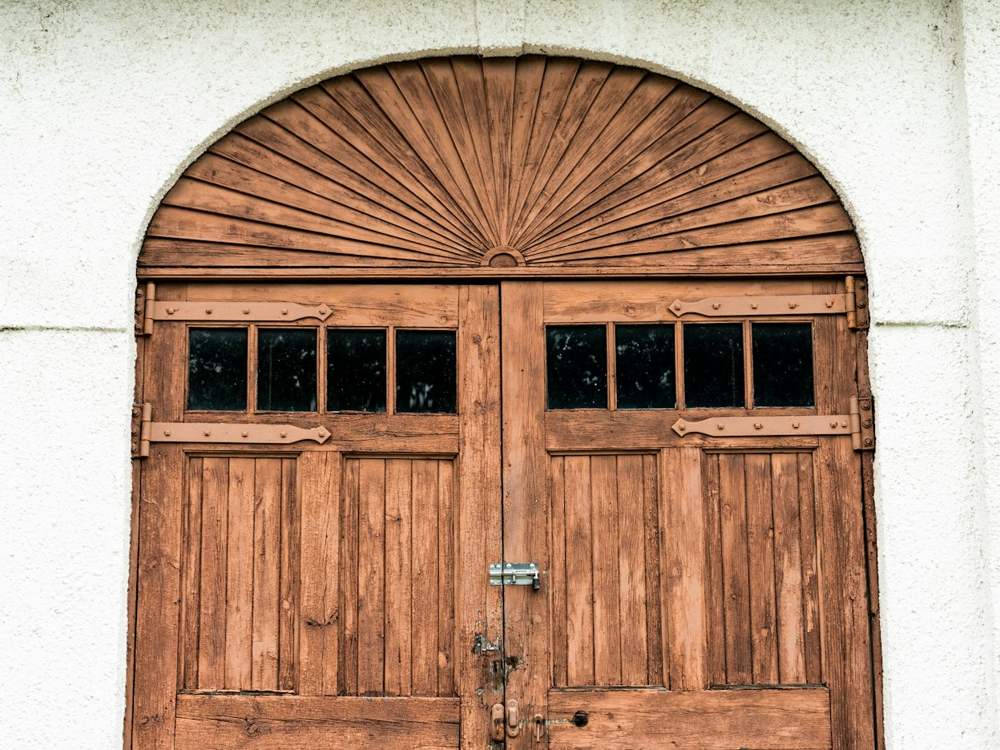 Porte de garage battante en bois à deux vantaux, cintrée, avec des carreaux en partie haute