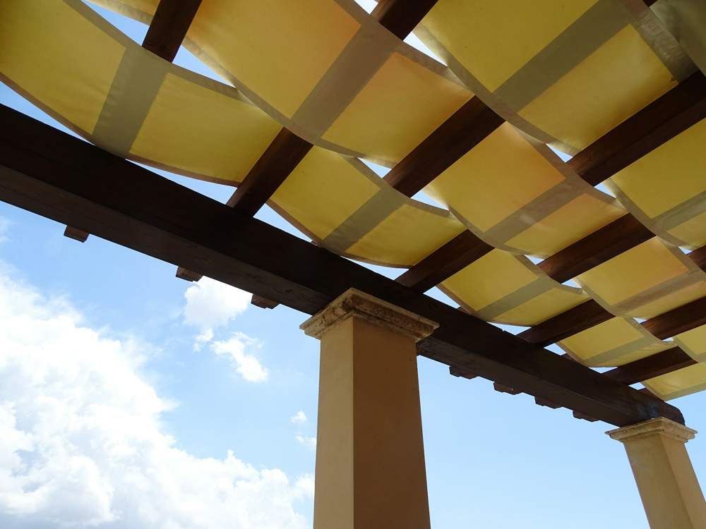 Toiles jaunes tendues en vagues entre les poutres d’une pergola en bois