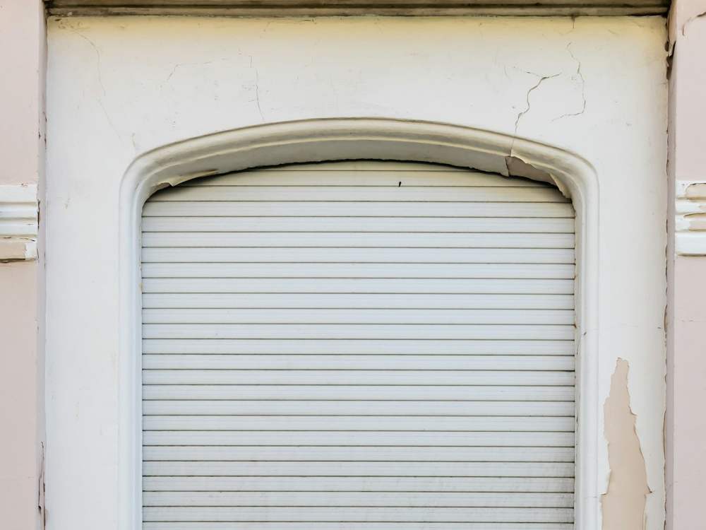 Volet roulant blanc fermé dans une fenêtre cintrée d’un immeuble ancien
